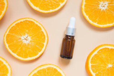 Doğal C vitamini serumu, cilt bakımı, temel yağ ürünleri. Kozmetik kahverengi cam şişe ve turuncu arka planda taze portakal suyu dilimi. Güzellik ürünleri markası maketi. Üst görünüm.