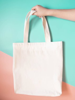 Boş beyaz çanta bez kumaş ve kabzası da tasarım. Yeşil turuncu arka planda kadın el ele tutuşması ya da tekrar kullanılabilir alışveriş torbası. Plastik poşet ve ekoloji konsepti yok. Boşluğu kopyala.