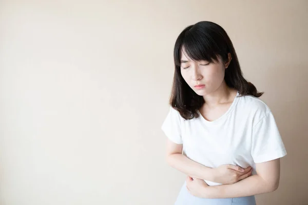 Young asian woman suffering form stomach ache over white background w/ copy space. Causes of abdominal pain include menstruation pain, gastritis, stomach ulcer, food poisoning, diarrhea or IBS.