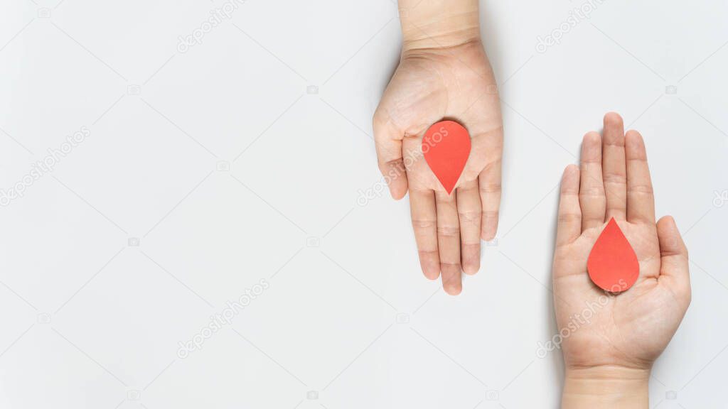 Blood donation - Human hand giving blood drop symbol to a hand on white background. World blood donor day and save life concept. Flat lay. Copy space.