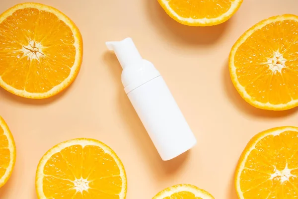 Natural vitamin c skincare products w/ fresh juicy orange fruit slice on orange background. Cosmetic beauty product branding mock-up for moisturizing cream, lotion, serum or essential oil. Top view.