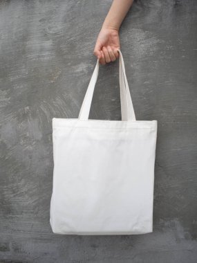 Boş beyaz çanta bez kumaş ve kabzası da tasarım. Grunge Gri Duvar 'da kadın el ele tutuşan eko ya da tekrar kullanılabilir alışveriş torbası. Plastik poşet ve ekoloji konsepti yok. Dikey.