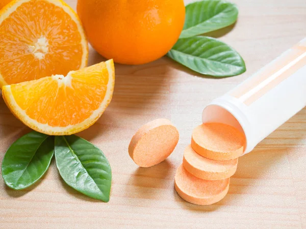 Beyaz plastik şişeden dökülen C vitamini tableti taze portakal meyveleri ve ahşap masa üzerinde yeşil yaprak. Yiyeceklerden ya da takviye malzemelerinden alınan vitaminler. Sağlık ve Tıp Konsepti.