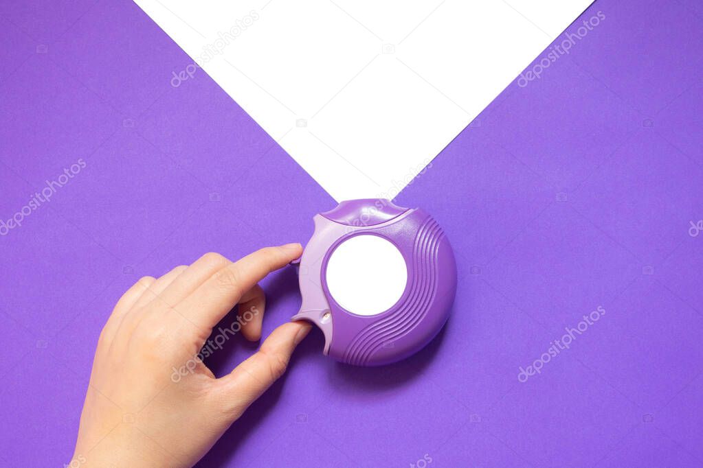 Asthma/COPD disease concept. Female hand open mouthpiece of medicine dry powder inhaler on purple white background. Pharmaceutical product for lung inflammation and prevent asthma attack. Minimal.