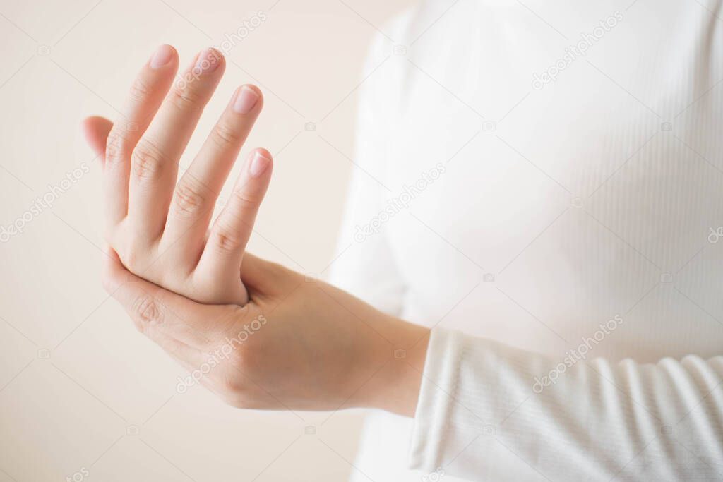 Young female in white t-shirt suffering from pain in hands and massaging her painful hands. Causes of hurt include carpal tunnel syndrome, fractures, arthritis or trigger finger. Copy space.
