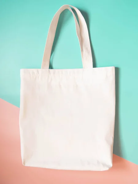 Mock up design bag concept. Blank white tote bag canvas fabric on orange green background. Empty eco bag. Copy space. Vertical.