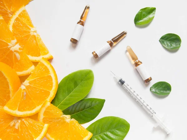 Enjeksiyon ve şırınga için C vitamini kahverengi ampulün üst görüntüsü taze portakal suyu dilimi ve beyaz masada yeşil yapraklar. Vitamin / mineral takviyesi konsepti. Güzellik ürünü maketi..