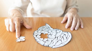 Yaşlı kadın elleri, kayıp yapboz parçasını insan beyni şekline sokuyor. Hafıza kaybı, bunama, Alzheimer hastalığı ve akıl sağlığı konsepti için yaratıcı bir fikir.