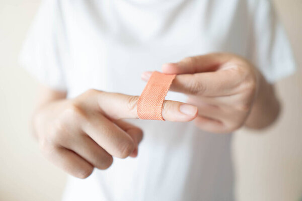 Young female in white t-shirt have injured index finger and putting adhesive bandages plaster for first aid. Health care and medical concept. Close up.;
