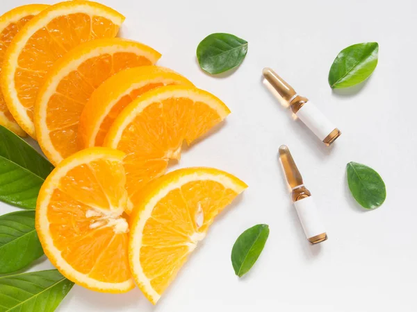Enjeksiyon için C vitamini kahverengi ampule beyaz masada taze portakal slaytları ve yeşil yapraklar. Vitamin sentetik ya da doğal beslenme seçimi konsepti. Güzellik ürünü maketi..