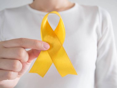 Endometriyozis, intihar önleme, sarkoma kemiği kanseri, mesane kanseri, karaciğer kanseri ve çocukluk kanseri konsepti için sarı altın kurdele farkındalığı sembolü taşıyan genç bir kadın. Sağlık hizmetleri. Kapat..