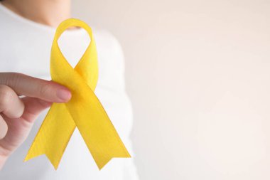Endometriyozis, intihar önleme, sarkoma kemiği kanseri, mesane kanseri, karaciğer kanseri ve çocukluk kanseri konsepti için sarı altın kurdele farkındalığı sembolü taşıyan genç bir kadın. Sağlık hizmetleri. Boşluğu kopyala.