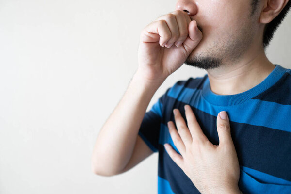 Young ill man have a cough and sore throat over white background. Causes of cough include pneumonia, bronchitis, allergy, asthma, COPD, TB or respiratory tract infection. Copy space. Health care.