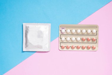 Doğum kontrol seçenekleri. Açık mavi arka planda hamileliği önlemek için prezervatif paketi ve oral hormonal doğum kontrol hapları. Aile planlaması, cinsel ve üreme sağlığı konsepti.