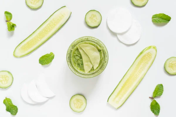 Cucumber eyes mask or makeup remover pads made with natural ingredients for healthy skin care. Top view of cucumber slice, mint leaf, facial cotton pad and jar on white table. Homemade beauty product.