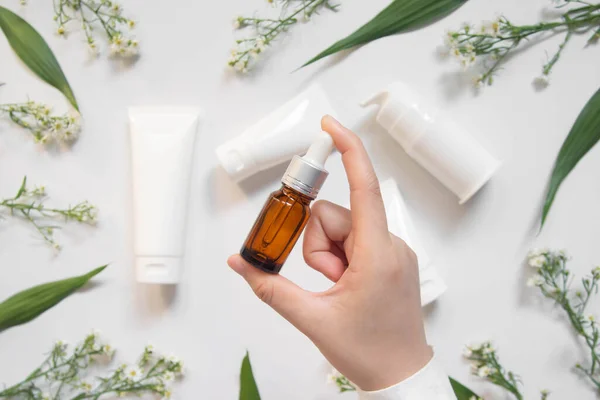 Serum veya temel yağ w / organik bitkisel özüt. Kadının elinde kahverengi cam şişe ve beyaz arka planda doğal cilt bakımı şişeleri var. Doğal güzellik kozmetik ürünü. Üst görünüm.