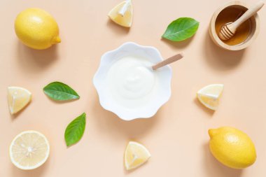 Parlak ve sağlıklı cilt için mükemmel ev yapımı doğal yüz maskesi malzemeleri. Yoğurt manzaralı, turuncu arka planda limon ve bal. Güzellik bitkisel cilt ürünü konsepti. Düz yatıyordu.