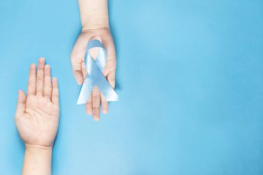 Erkek sağlığı ve prostat kanseri farkındalığı kampanyası konsepti. İnsan elleri, açık mavi kurdele farkındalığı sembolize ediyor ve gökyüzünde kanser olarak yaşayan insanlara yardım ve destek oluyor. Boşluğu kopyala.