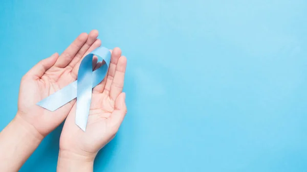 男子健康与前列腺癌意识运动于11月展开 人的手在蓝天的背景上握住浅蓝色的丝带 支持那些患有W 癌症的男人的符号 复制空间 — 图库照片