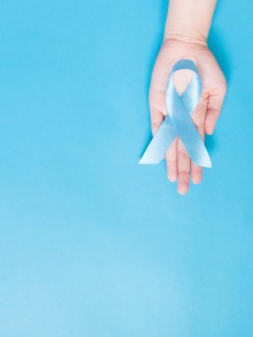 Erkek sağlığı ve prostat kanseri farkındalığı kampanyası konsepti. Mavi arka planda açık mavi kurdele tutan adam elleri. Kanser yaşayan erkeklere destek için bir sembol. Uzayı kopyala Dikey.