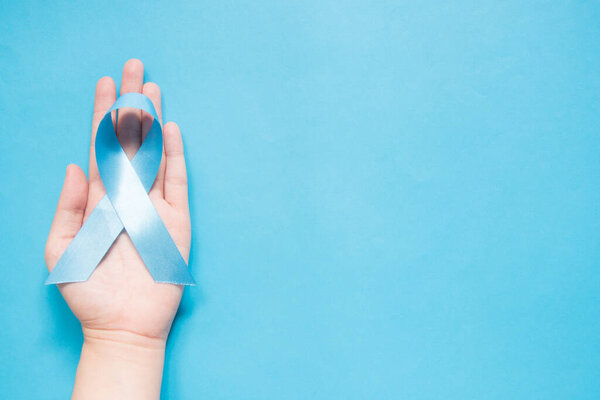 Men 's health and Prostate cancer awareness campaign in November. Мужские руки держат светло-голубую ленточку осознания на голубом фоне. Символ поддержки мужчин, живущих с раком. Копирование пространства.