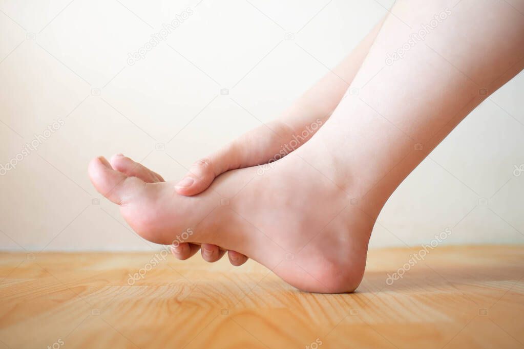 Young female suffering from foot pain or numbness at home. Causes of pain include plantar fasciitis, gout, arthritis, tendinitis, diabetic neuropathy or overuse injuries. Healthcare concept. Close up.
