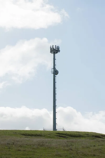 空と雲の後ろに草の上の携帯電話の塔 — ストック写真