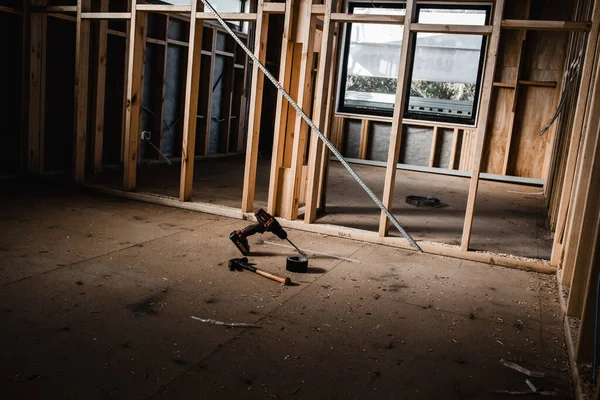 A construction set of a house being built with exposed wires and wooden beams, light shining in on the tools