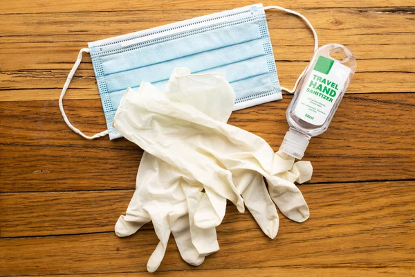 A blue disposable mask, cream disposable latex gloves and travel sized hand sanitzer on a wooden background of PPE used during the coronavirus COVID-19 pandemic