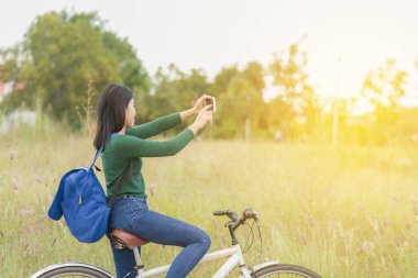 Bisikletli genç bir kadın doğadayken selfie çekiyor.