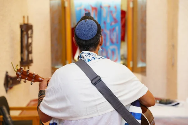 Rabbi der jüdischen Reformbewegung ist in einen Tallit gehüllt, betet und spielt Gitarre vor der Thora-ARK. — Stockfoto