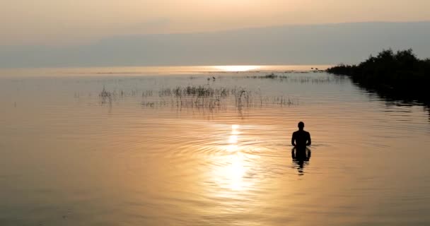 Homem mergulhado na água do lago Galiléia em Israel ao nascer do sol. — Vídeo de Stock