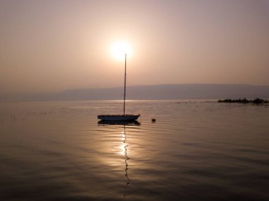 Gölün üzerinde gün doğumu. Gün batımında sakin sularda yüzen bir tekne..