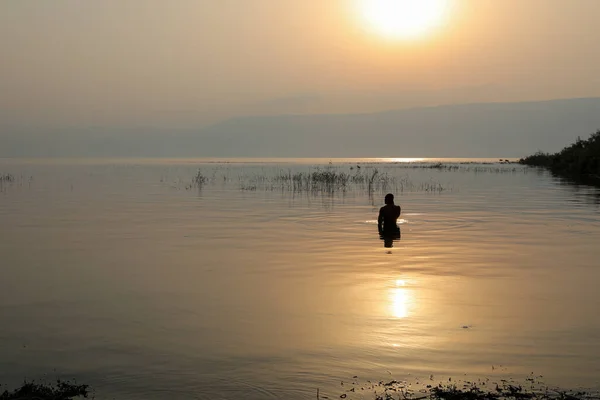 Man dipped in the water of Galilee Lake in Israel at sunrise.