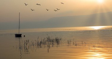 Gölün üzerinde gün doğumu. Gün batımında sakin sularda yüzen bir tekne..