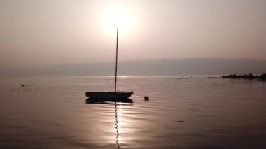 Gölün üzerinde gün doğumu. Gün batımında sakin sularda yüzen bir tekne..