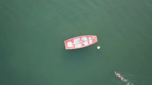 Man swimming towards a sailing boat moored at sea. Pull up drone shot. — Stock Video