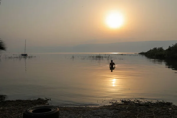 Az ember a Galileai-tó vizébe merült Izraelben napkeltekor.. — Stock Fotó