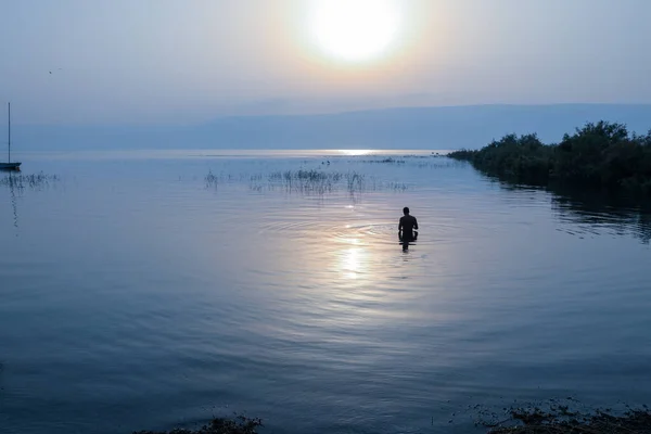 Az ember a Galileai-tó vizébe merült Izraelben napkeltekor.. — Stock Fotó