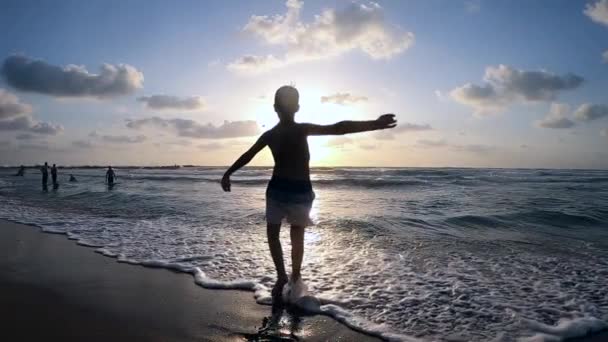美しい夕日を背景に石を海に投げ込む子供のシルエット. — ストック動画