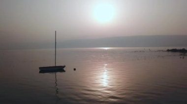 Gölün üzerinde gün doğumu. Gün batımında sakin sularda yüzen bir tekne..