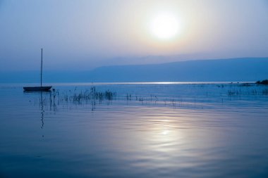 Gölün üzerinde gün doğumu. Gün batımında sakin sularda yüzen bir tekne..