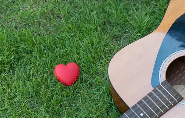 Soyut aşk ve müzik konsepti. Yeşil tarlalarda kırmızı kalp ve gitar. Hobi ve müzik rahatlatıcı konsept.