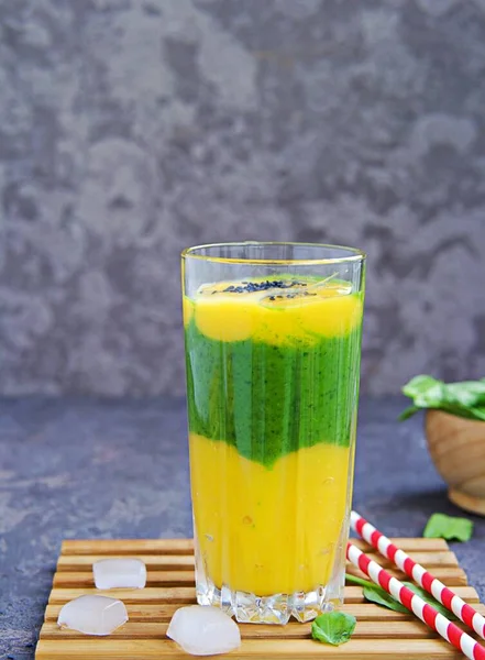 A healthy drink, a three-layer smoothie with fresh spinach and ripe mango in a tall glass glass on a dark concrete background. Drinks for detox and weight loss. Refreshing non-alcoholic cocktails.