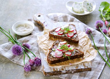 Üçgen çavdar ekmeğinde sandviç, bitkisel tereyağı ve tahta üzerinde taze turp, gri beton arka planda..