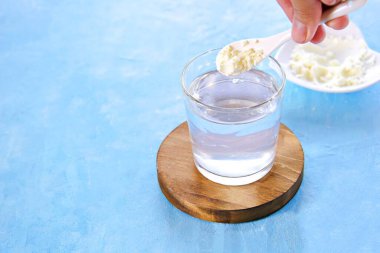 Pudralanmış kolajen ve mavi beton arka planda bir bardak su..