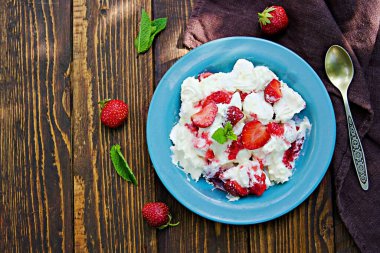 Et karışımı olarak bilinen tatlı, çıtır krema, çırpılmış krema ve ahşap arka planda mavi bir tabakta taze çilek. Çilek tarifli tatlılar. İngiliz mutfağı.