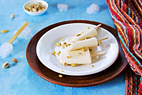 Three portions of the Indian kulfi ice cream with cardamom and pistachios on a white plate on a blue background concrete. Traditional indian ice cream. Indian food.