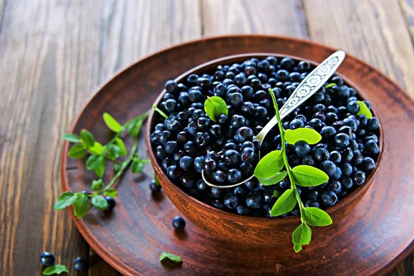 Fresh wild blueberries in a clay brown bowl on a wooden background. Healthy food, snacks. Selective focus