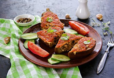 Patlıcan dilimlenmiş tavuk, peynir ve domates sosuyla doldurulmuş siyah beton arka planda kahverengi kil tabakta. Patlıcan Tarifleri